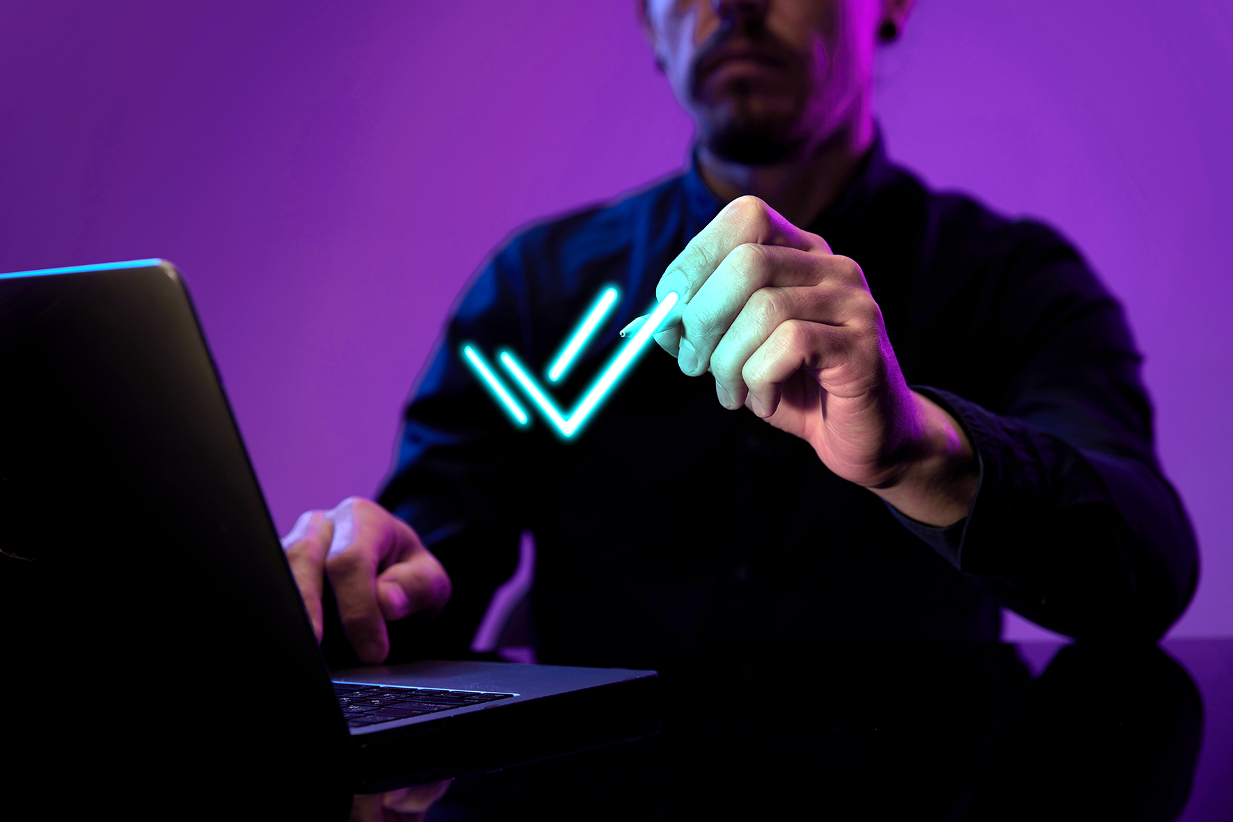 Man in front of laptop making virtual check marks, purple, neon