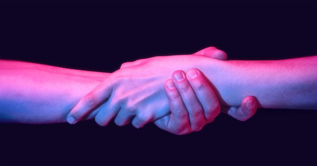 Close up handshake, black background, pink hue