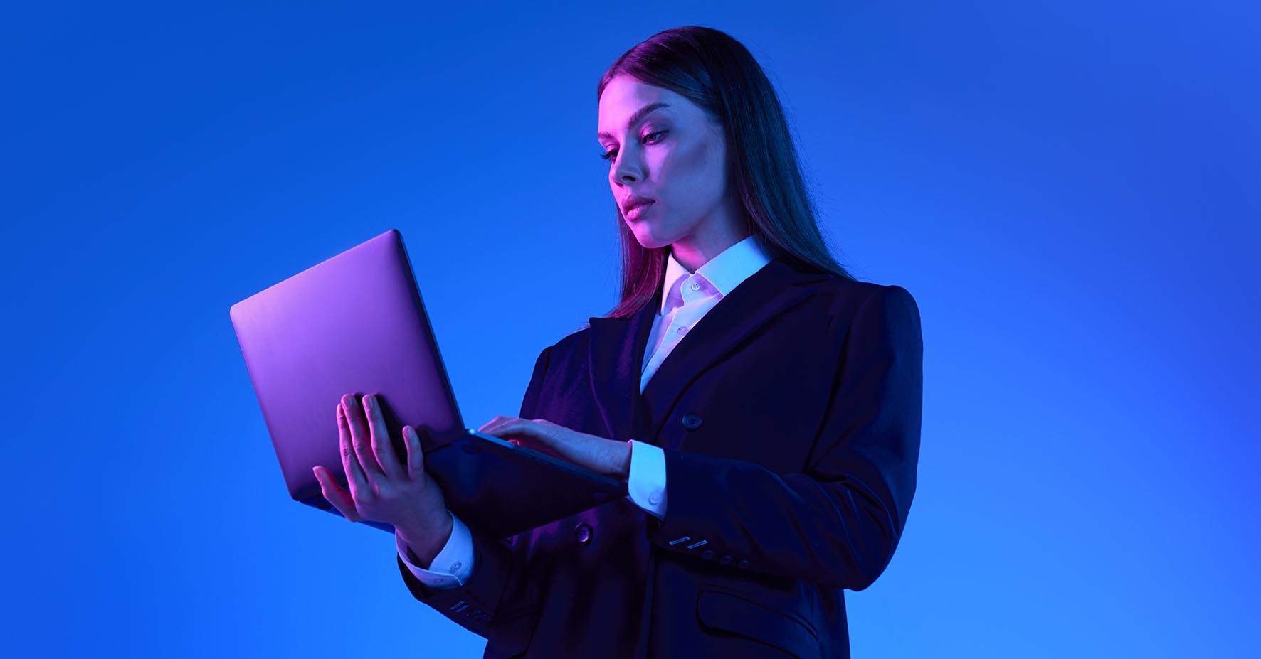 Woman in suit standing using computer, blue background